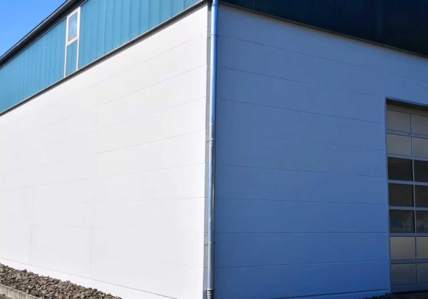 Fugentechnik Buchen - Bau - Außenecke eines modernen Industriegebäudes mit weißen und blauen Paneelen und einer Steinreihe am Sockel