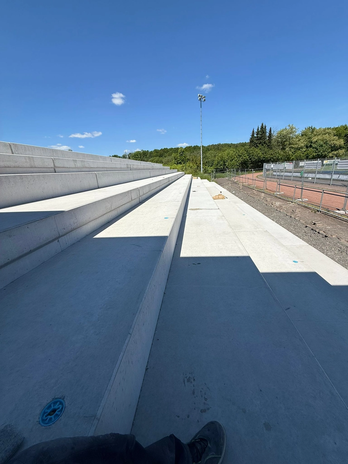 Fugentechnik Buchen – Bau – Betontribüne unter klarem, blauem Himmel mit Bäumen und einem Lichtmast im Hintergrund
