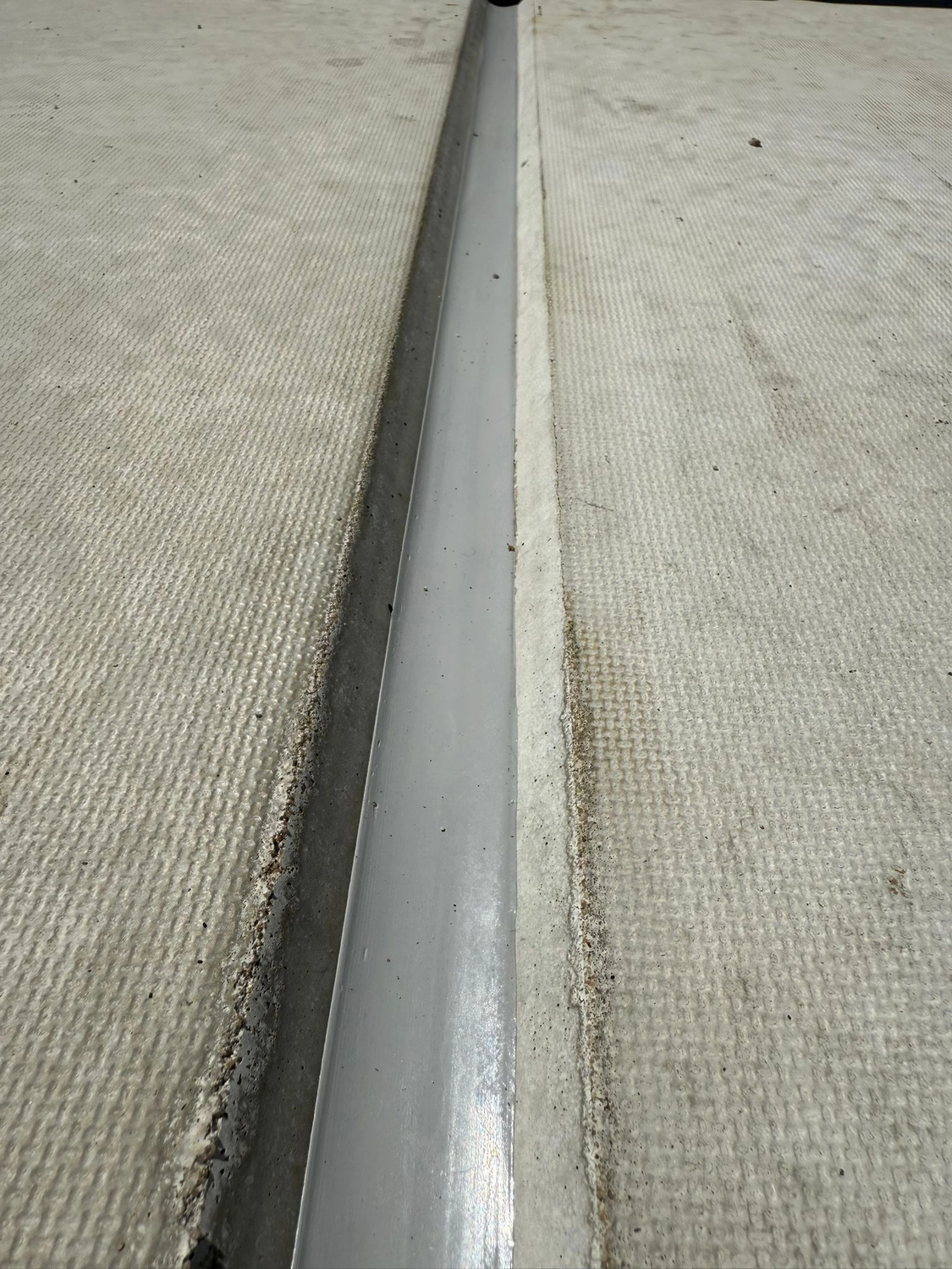 Fugentechnik Buchen - Bau - Nahaufnahme eines schmalen Metallprofils, das zwischen zwei Abschnitten strukturierter, heller Dachbahnen eingelassen ist