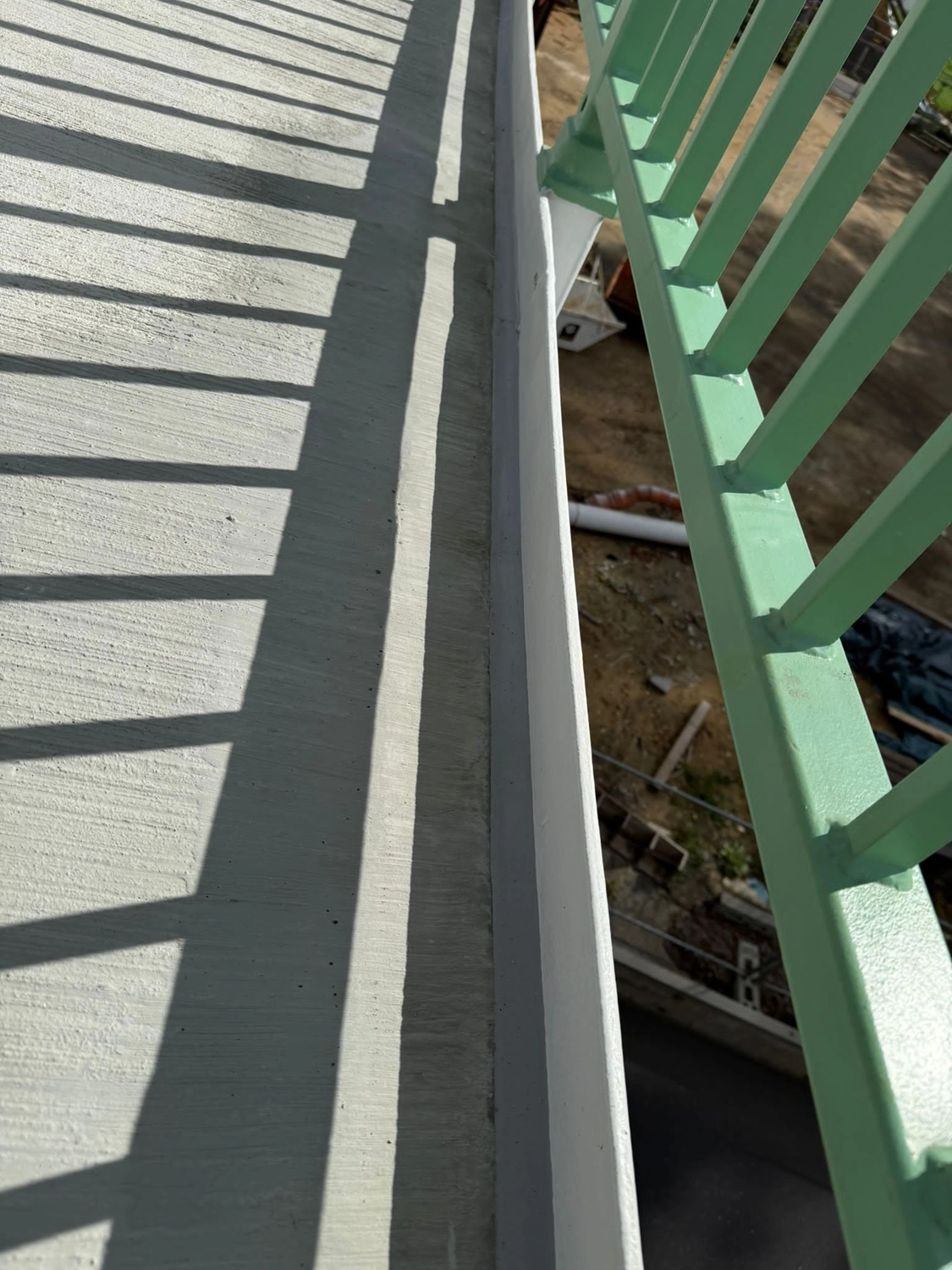 Fugentechnik Buchen - Bau - Grünes Metallgeländer wirft Schatten auf einen Betonbalkonboden mit Blick auf einen darunterliegenden Außenbereich