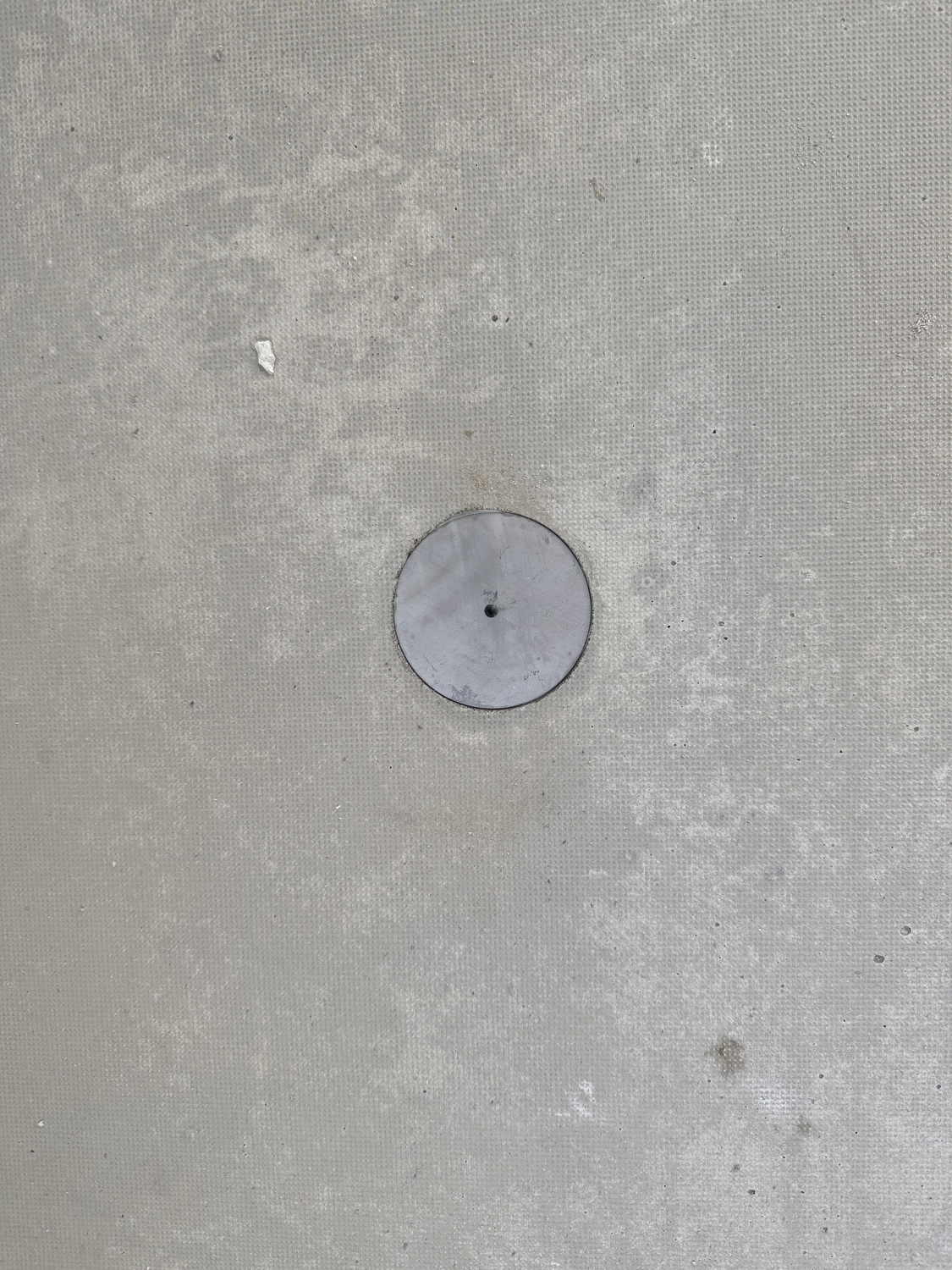 Fugentechnik Buchen - Bau - Runde Metallabdeckung, eingelassen in eine strukturierte Betonoberfläche mit einem kleinen zentralen Loch