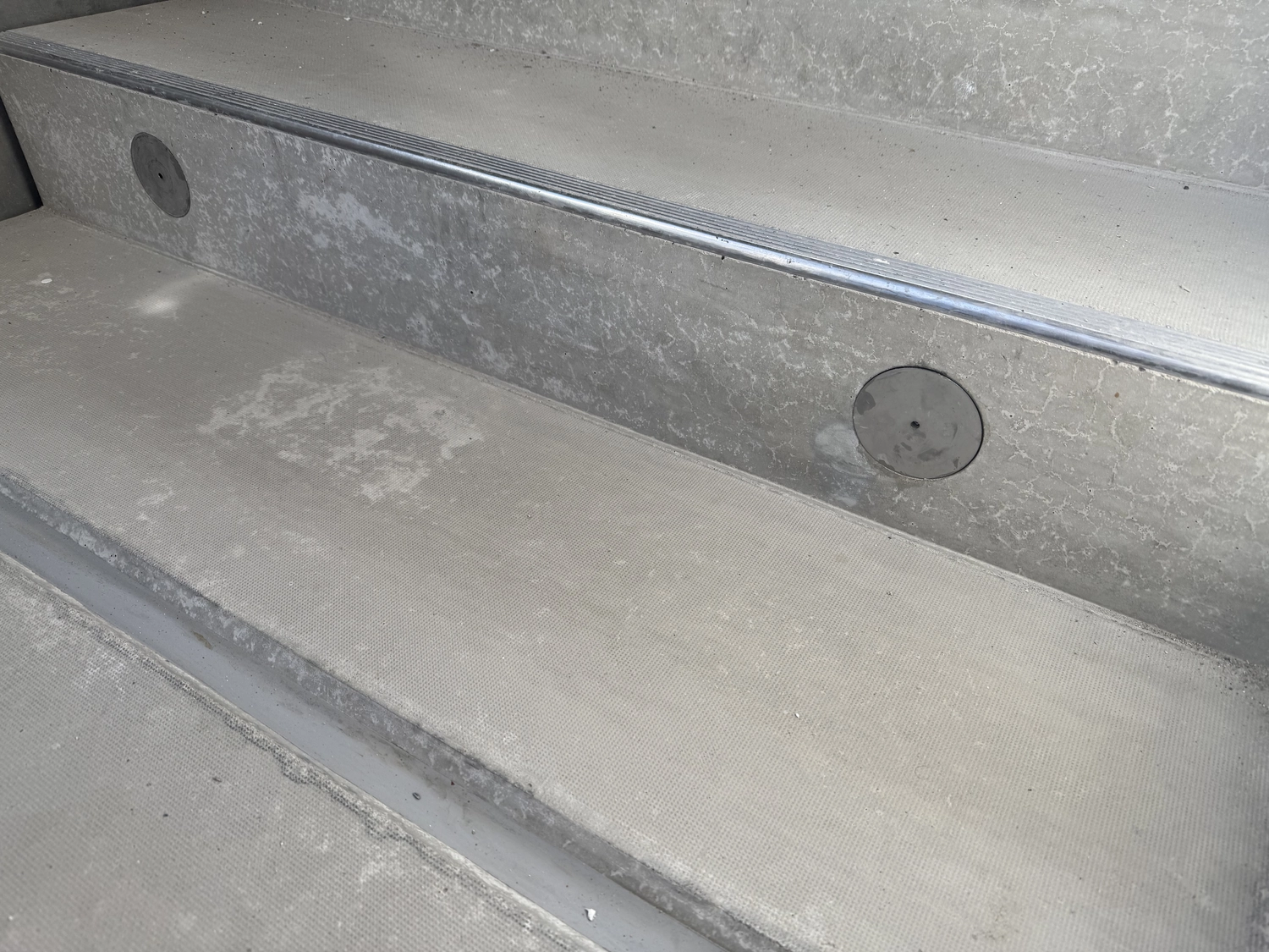 Fugentechnik Buchen - Bau - Nahaufnahme einer grauen Betontreppe mit strukturierter Trittfläche und runden Abflusslöchern