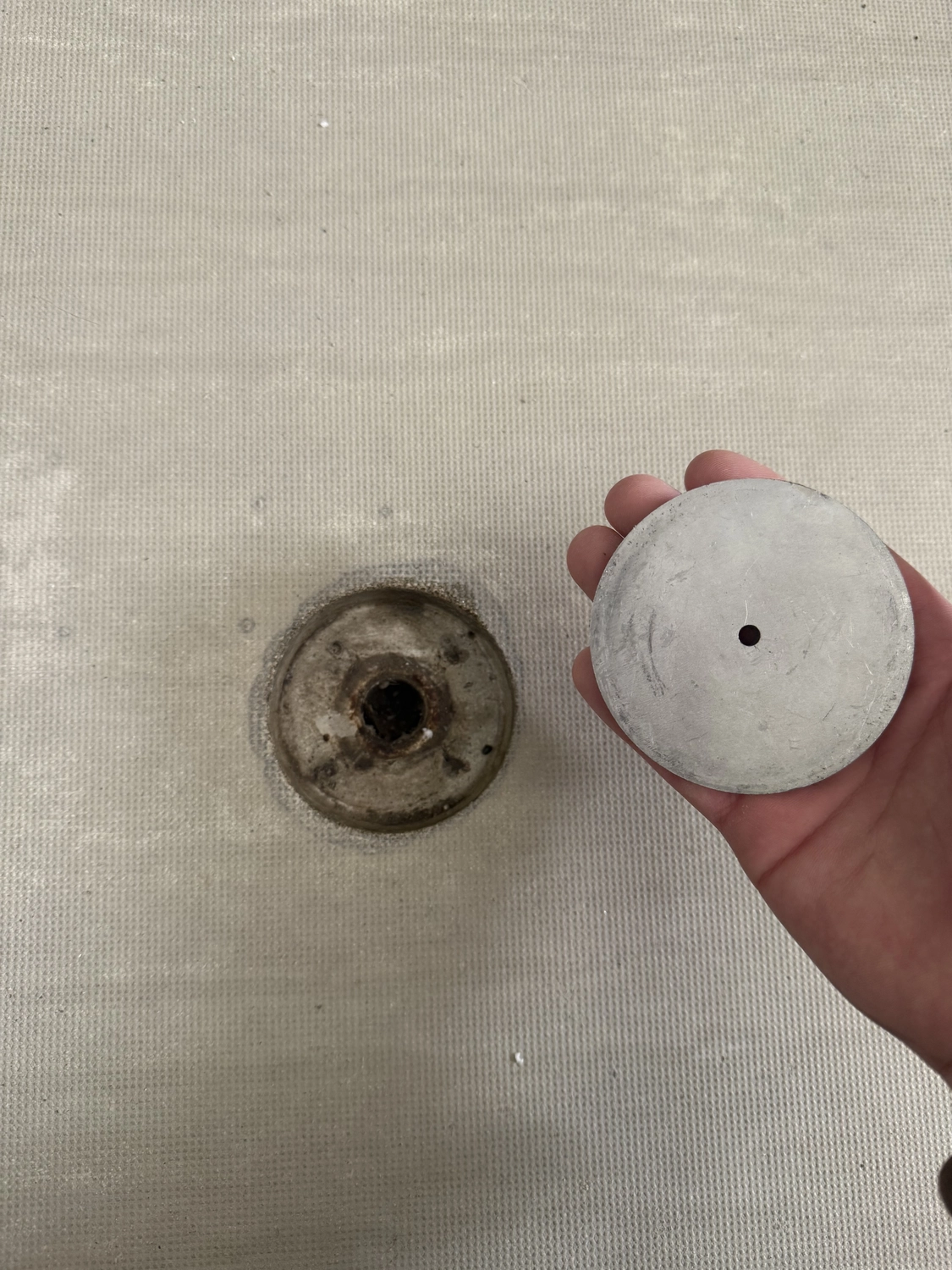 Fugentechnik Buchen - Bau - Hand hält einen runden Metallgegenstand mit einem kleinen Loch in der Mitte neben einer ähnlichen Vertiefung auf einer strukturierten beigen Oberfläche