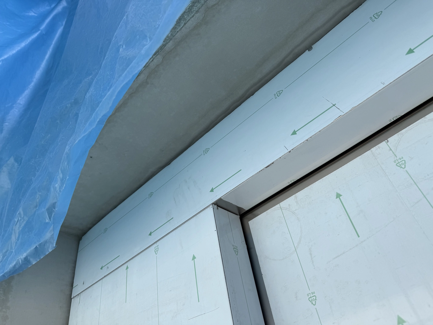 Fugentechnik Buchen - Bau - Nahaufnahme eines Eckabschnitts einer Metallpaneelinstallation, wobei die obere linke Ecke teilweise mit einer blauen Schutzfolie abgedeckt ist.