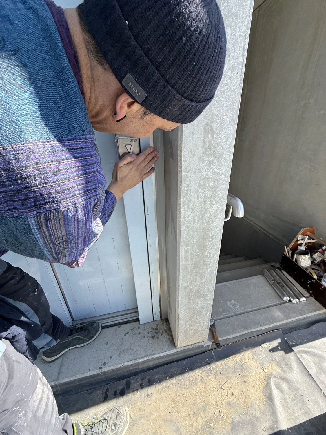 Fugentechnik Buchen - Bau - Person mit Strickmütze und buntem Pullover inspiziert einen Tür- oder Fensterrahmen neben einer Betonsäule in einem Innenraum
