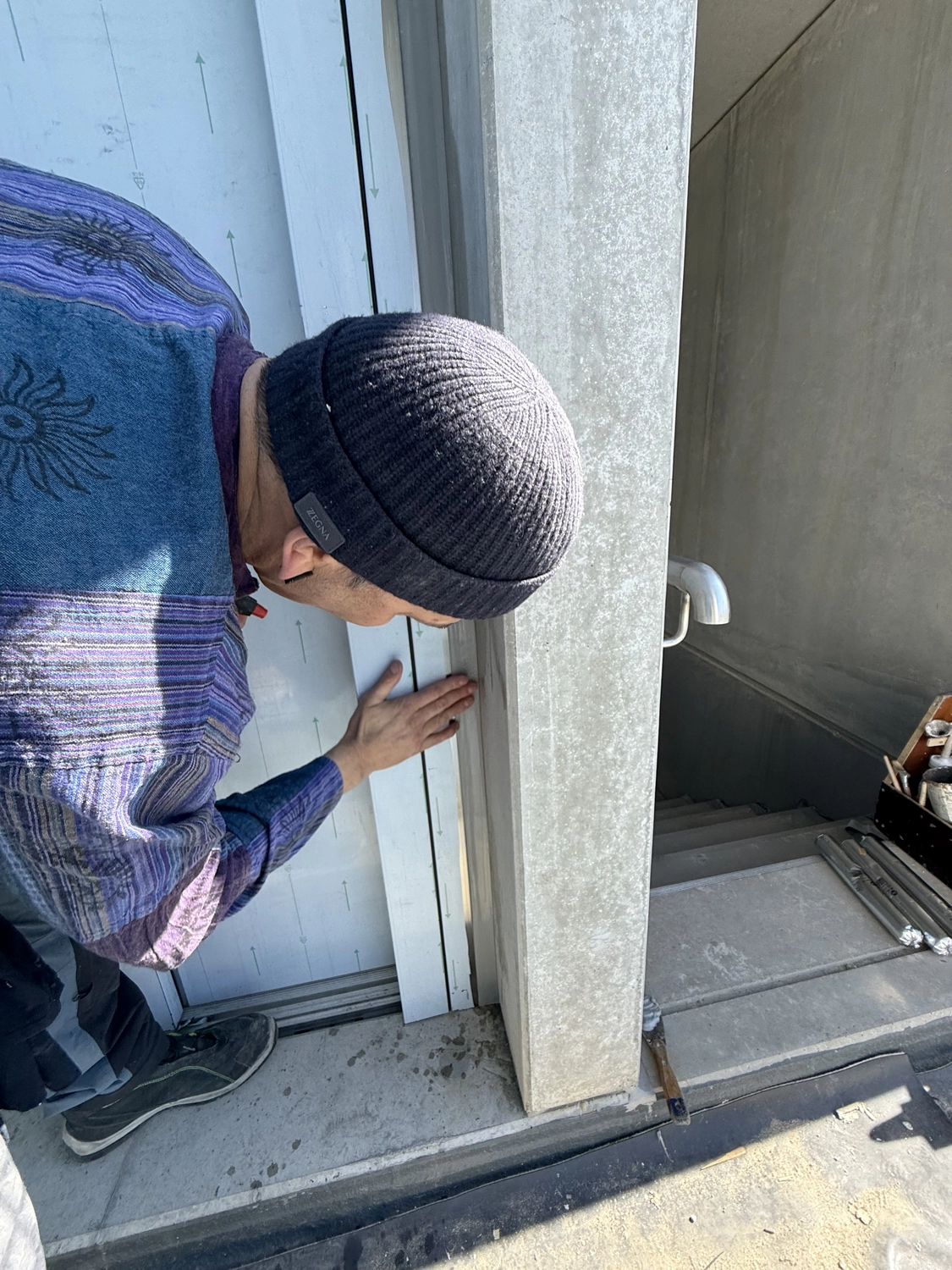 Fugentechnik Buchen - Bau - Person mit Strickmütze und buntem Pullover inspiziert einen Tür- oder Fensterrahmen neben einer Betonsäule in einem Innenraum