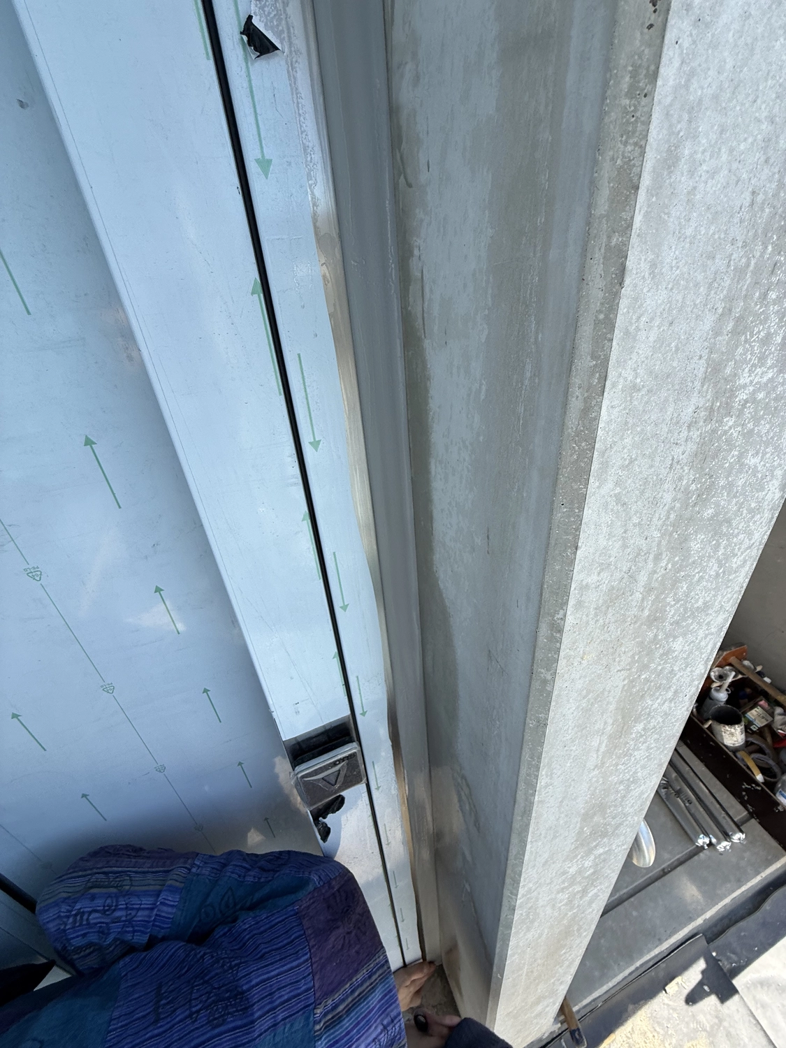 Fugentechnik Buchen - Bau - Nahaufnahme einer Person, die neben einer Betonwand eine Tür mit Schutzfolie und einem metallischen Türrahmen montiert oder justiert