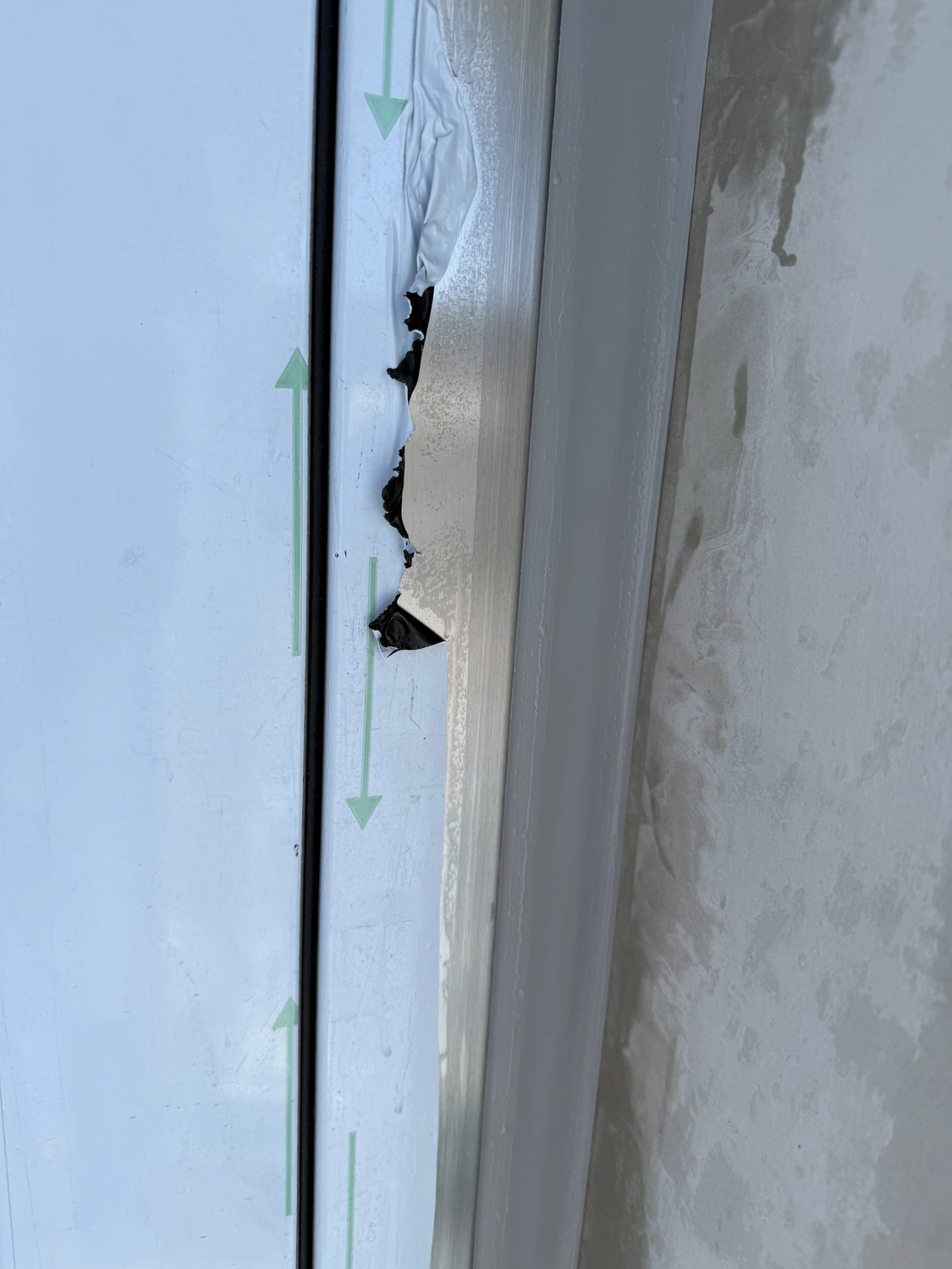 Fugentechnik Buchen - Bau - Nahaufnahme von beschädigtem und abblätterndem Dichtmittel an einem Fensterrahmen mit grünen Richtungspfeilen auf dem blau getönten Glas