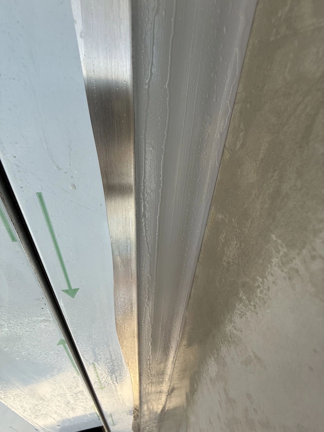 Fugentechnik Buchen - Bau - Nahaufnahme einer mattierten Glasscheibe mit Metallrand und Kondenswassertropfen auf einer beigefarbenen Fläche daneben
