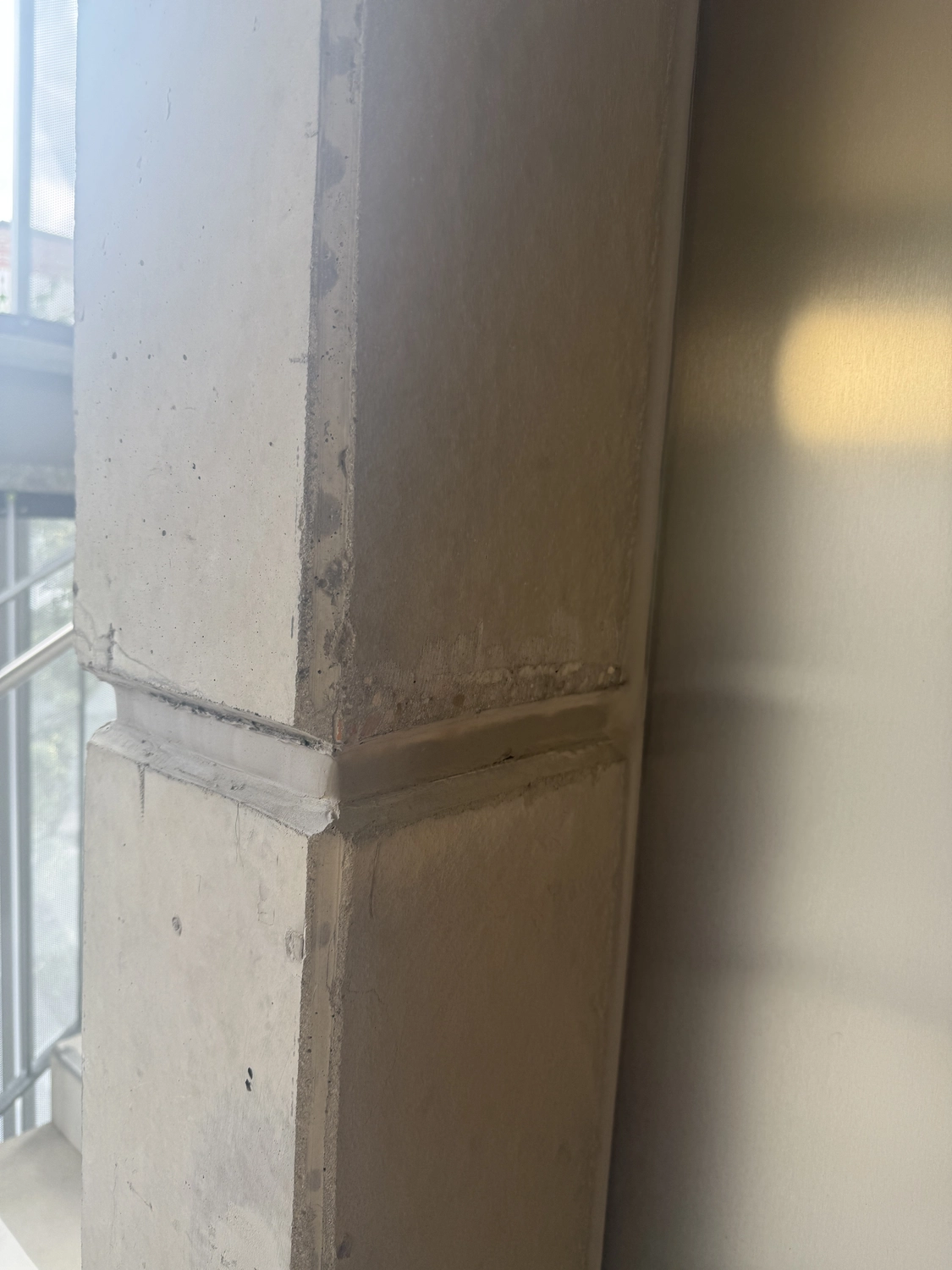 Fugentechnik Buchen - Bau - Nahaufnahme eines beigen Beton-Eckpfeilers mit sichtbaren Fugen und einer glatten Wand, die rechts das Licht reflektiert