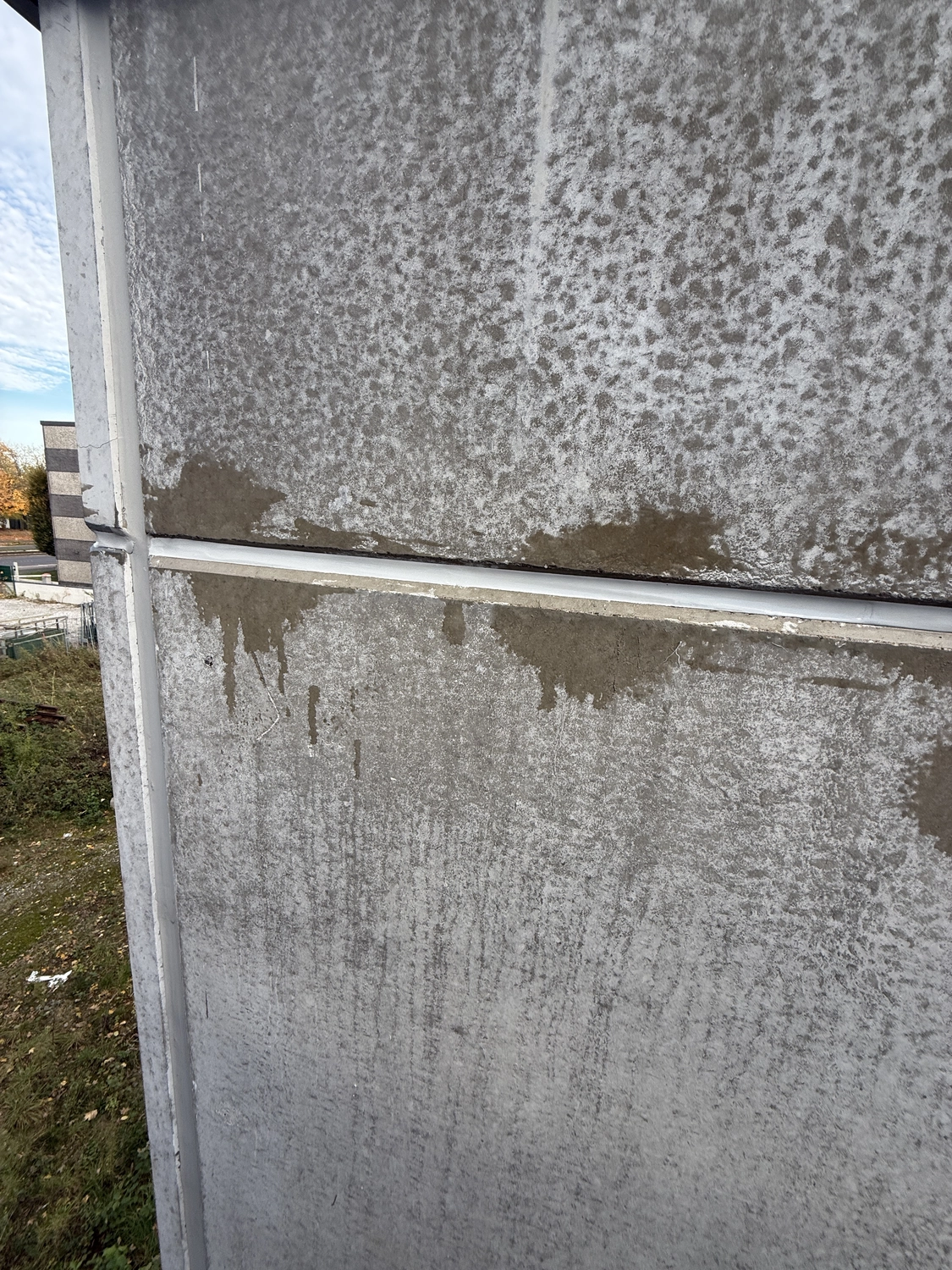 Fugentechnik Buchen - Bau - Nahaufnahme einer Betonwand mit verwitterter, fleckenartiger Verfärbung und einer weißen horizontalen Zierleiste in der Nähe der Mitte