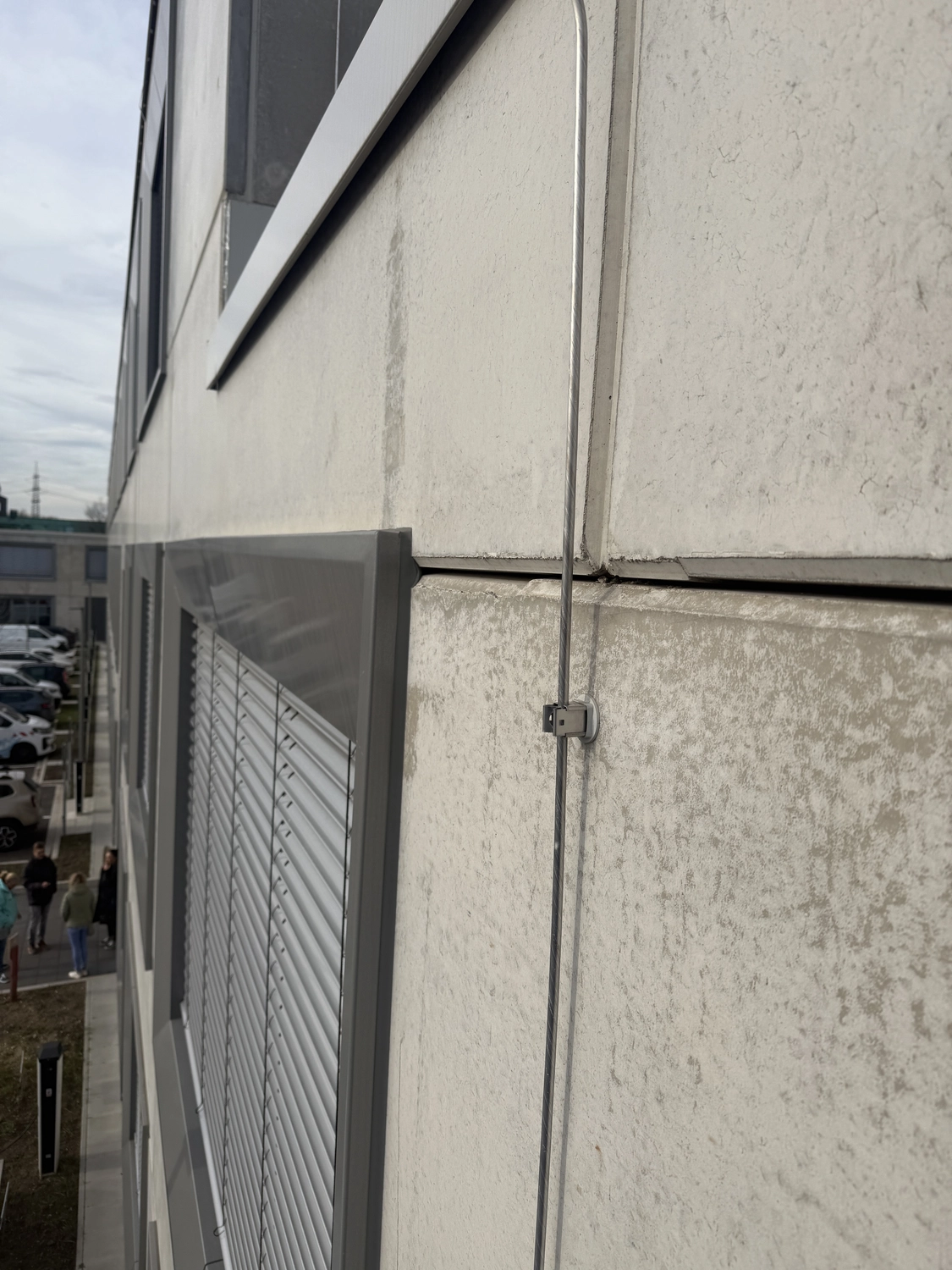 Fugentechnik Buchen - Bau - Nahaufnahme einer Gebäudefassade mit geschlossenen Metallfensterläden und einem vertikalen, an der Wand befestigten Metallseil