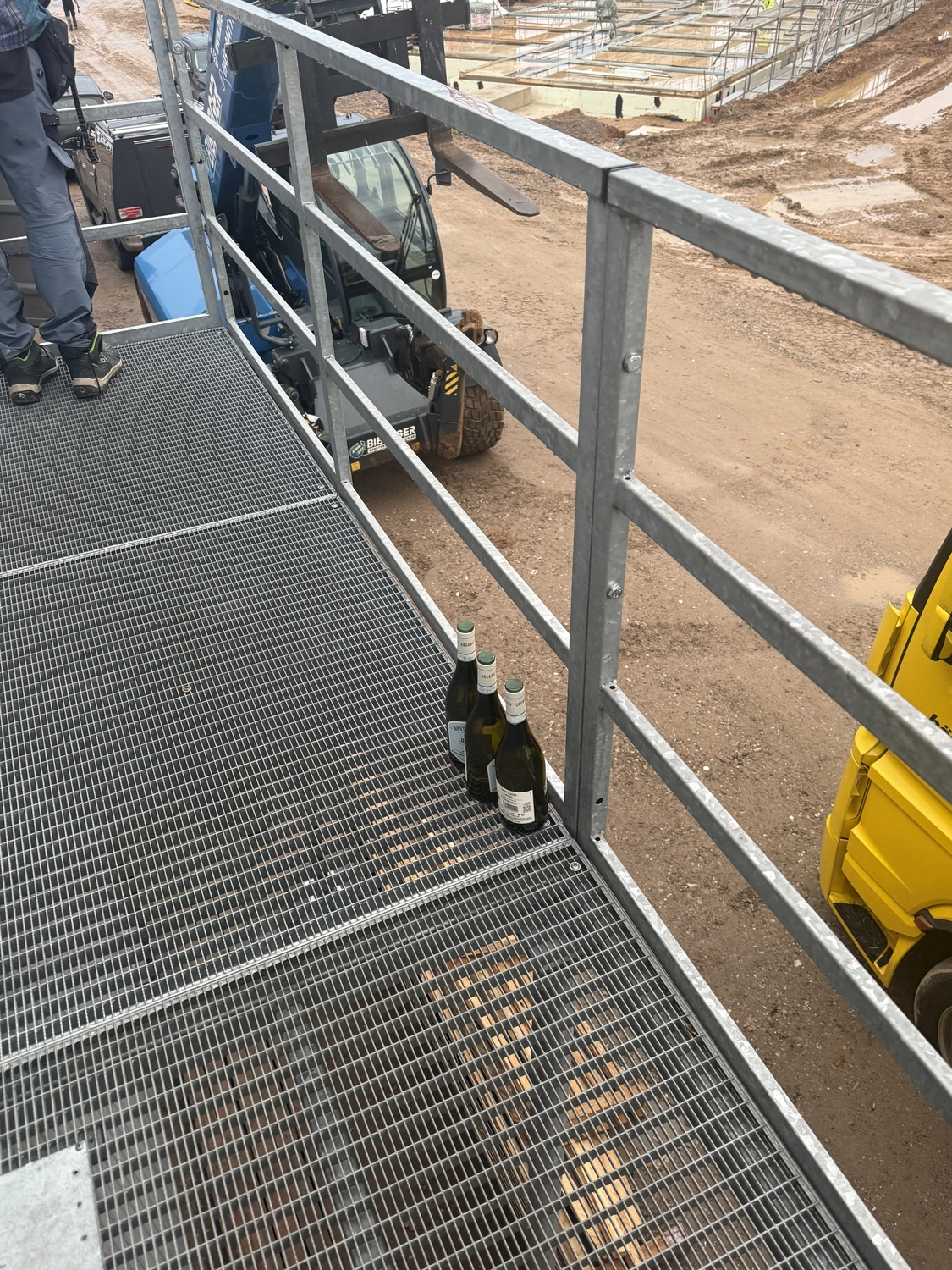 Fugentechnik Buchen - Bau - Drei Weinflaschen stehen auf einem Metallgitter auf einer Baustelle; darunter sind Maschinen und der Erdboden zu sehen