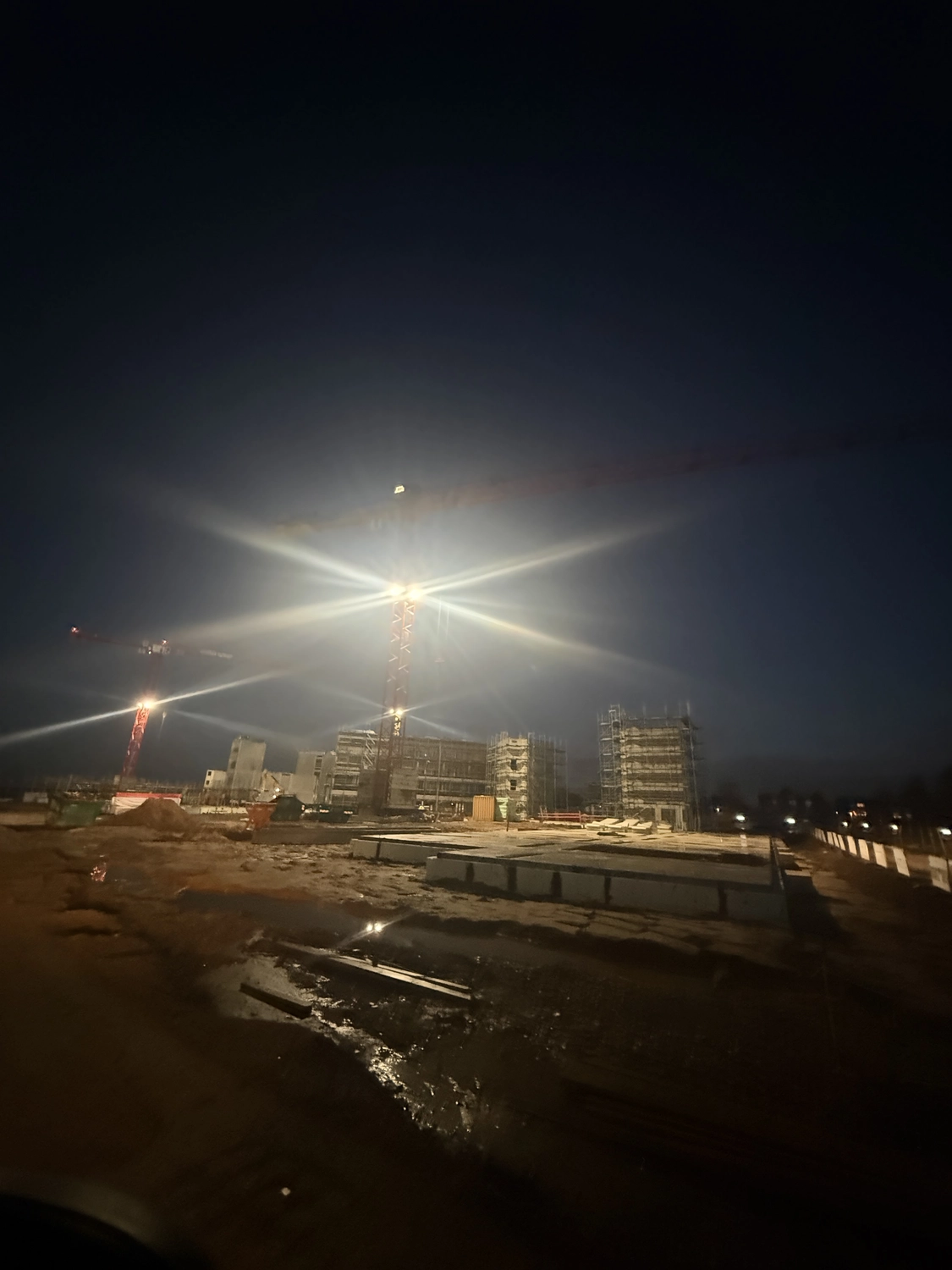 Fugentechnik Buchen - Bau - Baustelle bei Nacht mit beleuchteten Kränen und teilweise errichteten, von Gerüsten umgebenen Bauwerken