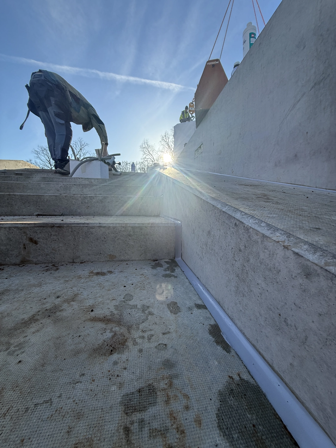 Fugentechnik Buchen - Bau - Person, die sich auf einer Betontreppe vorbeugt, im Hintergrund Sonnenlicht und blauer Himmel