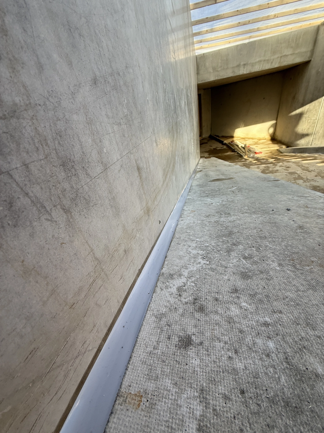 Fugentechnik Buchen - Bau - Innenbaustelle mit unfertigen Betonwänden und -boden, die einen schmalen Laufsteg unter einer Balkendecke zeigt