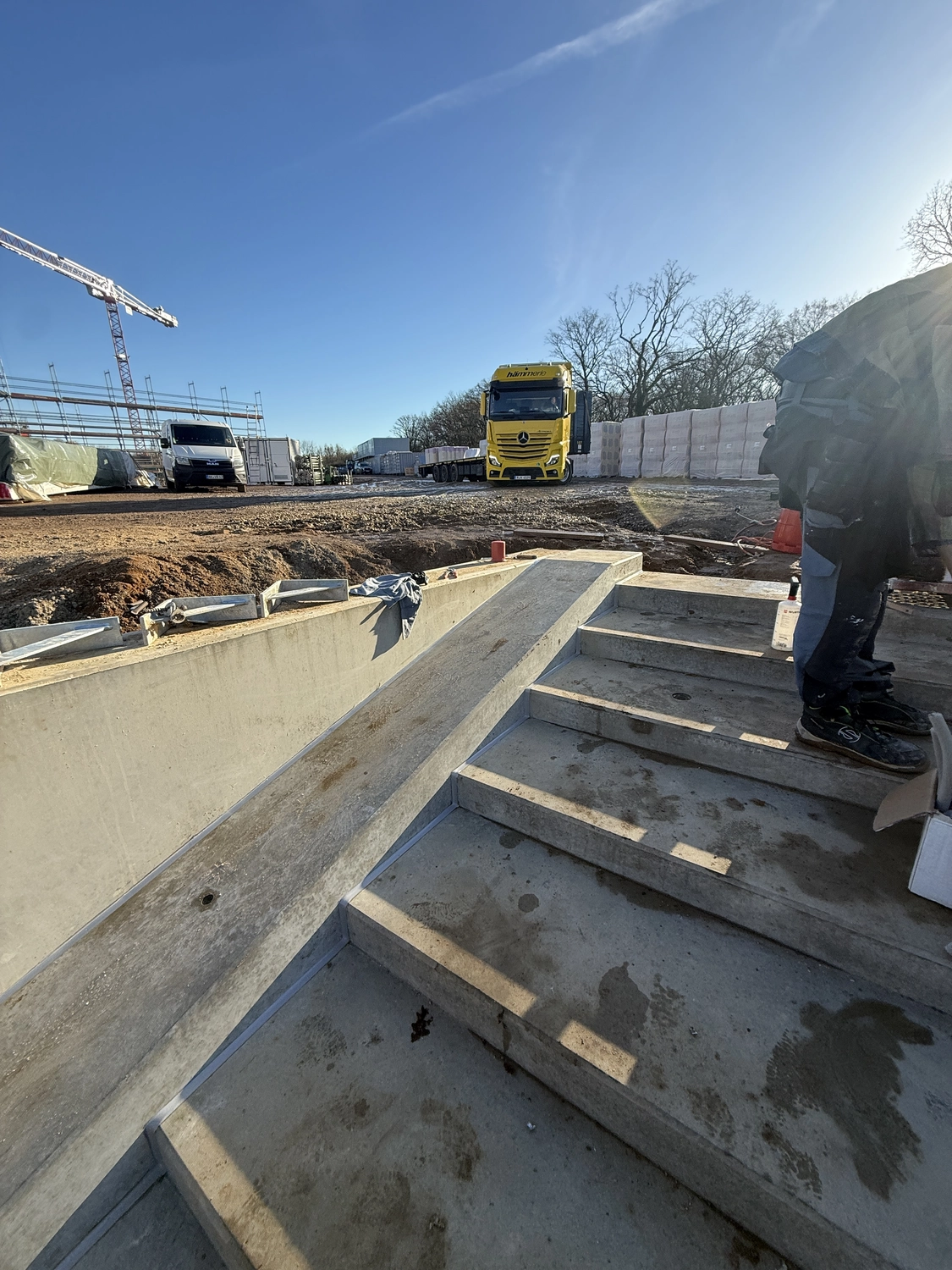 Fugentechnik Buchen – Bau – Betontreppe mit angrenzender Rampe auf einer Baustelle unter klarem, blauem Himmel, im Hintergrund ein gelber Lkw und weitere Fahrzeuge