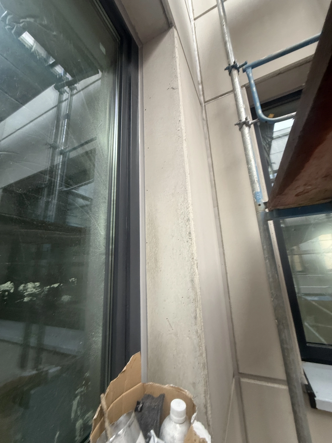Fugentechnik Buchen - Bau - Nahaufnahme eines Fensterrahmens mit einem sich im Glas spiegelnden Gerüst und einem daneben stehenden Karton mit Gegenständen