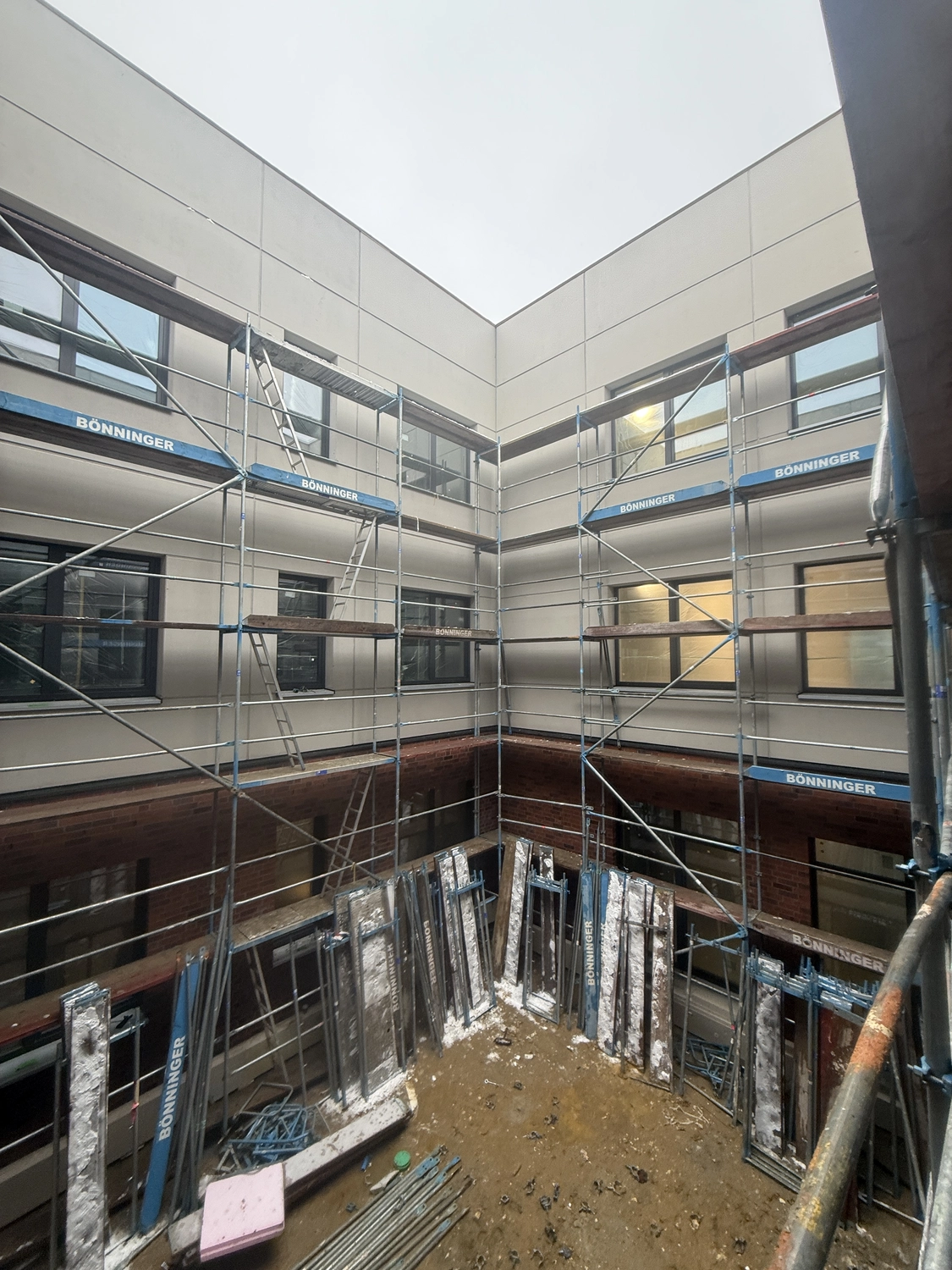 Fugentechnik Buchen - Bau - Baustelle im Innenhof eines dreistöckigen Gebäudes mit Gerüsten und an den Wänden lehnenden Glaspaneelen