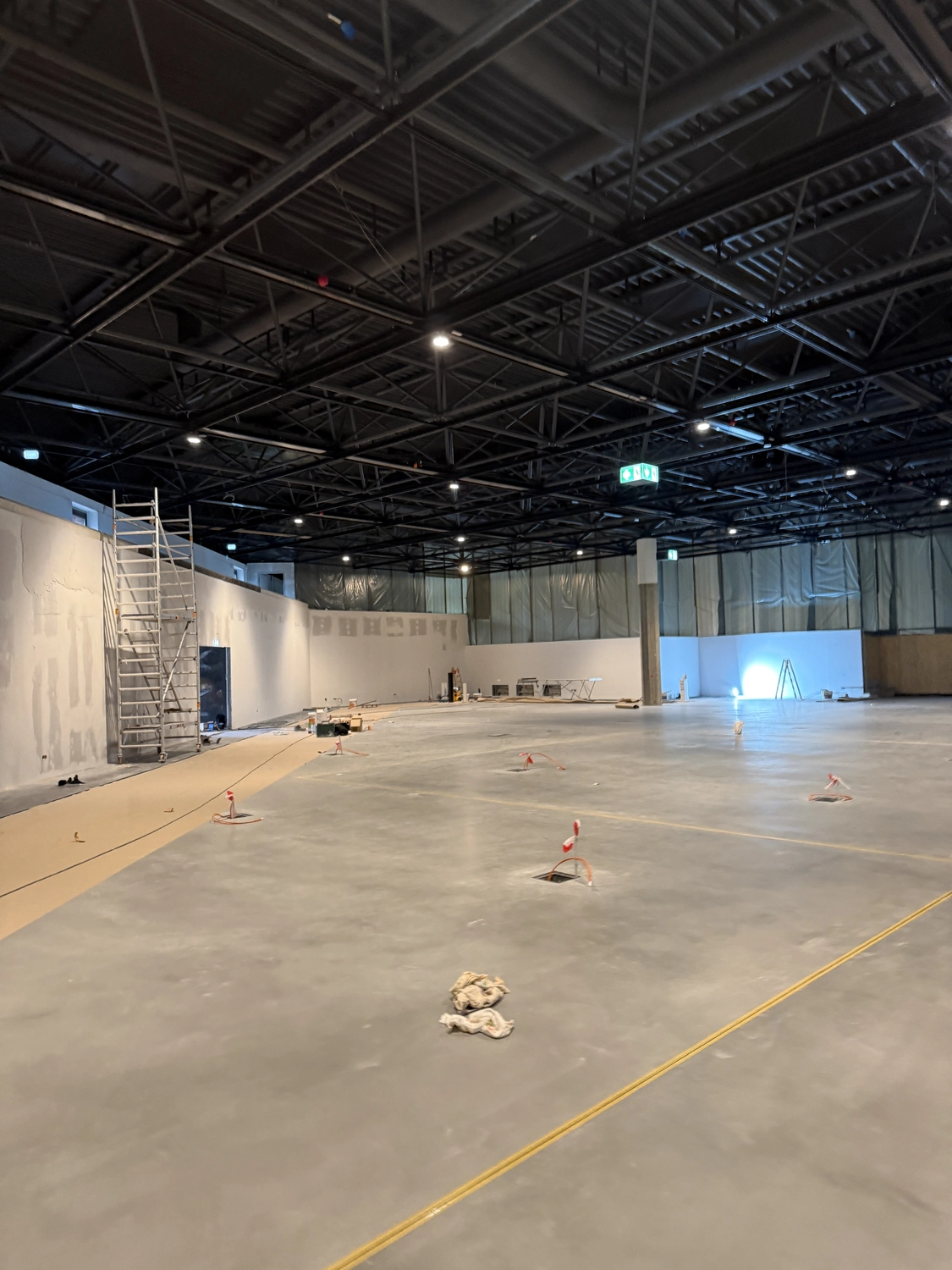 Fugentechnik Buchen – Bau – Große, im Bau befindliche Industriehalle mit glattem Betonboden, Gerüst und sichtbaren Deckenbalken mit Beleuchtung
