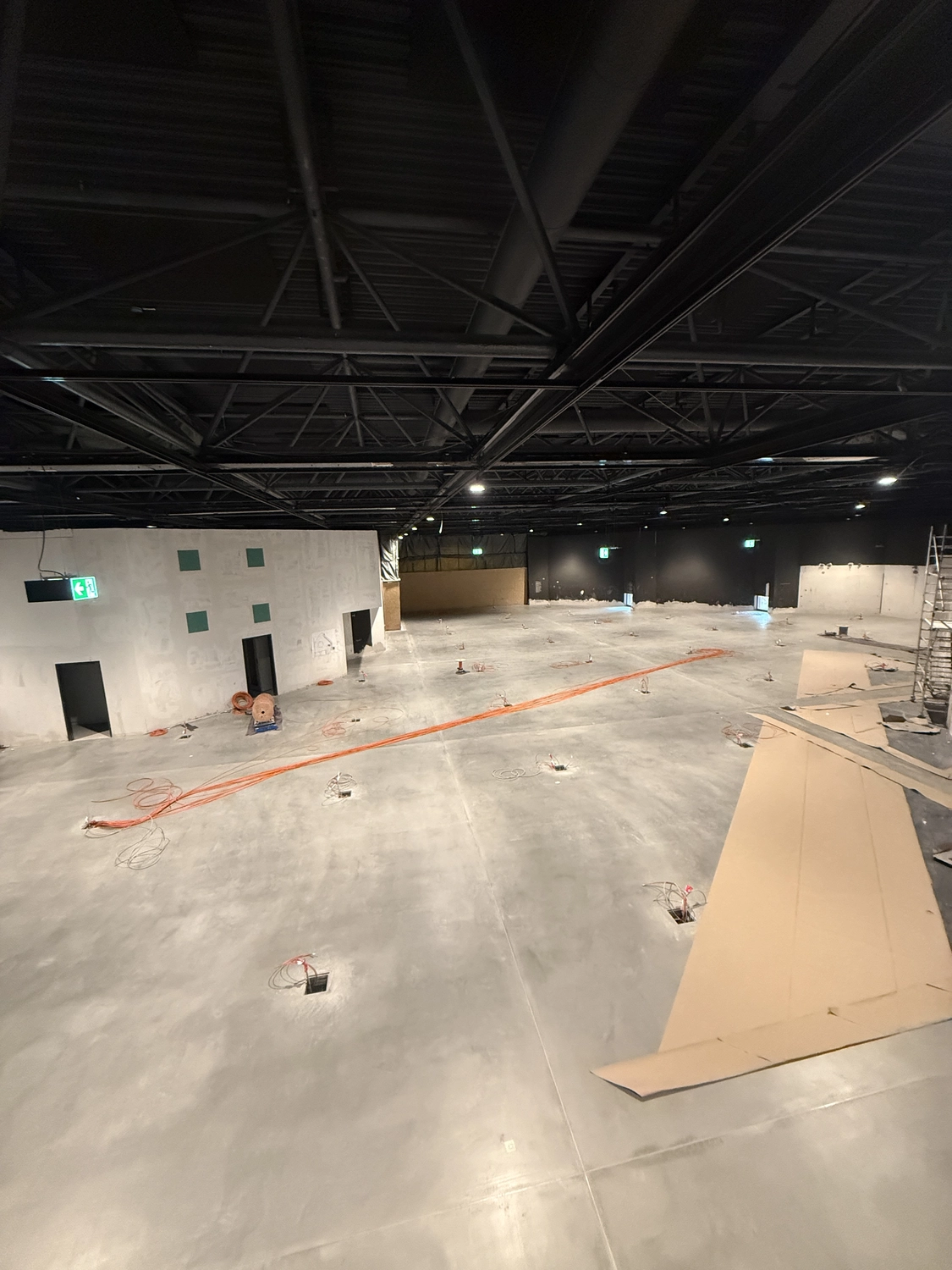 Fugentechnik Buchen – Bau – Große, leere Industriehalle im Bau mit freiliegenden Deckenbalken, Betonboden, verstreuten Kabeln und Sperrholzplatten auf dem Boden