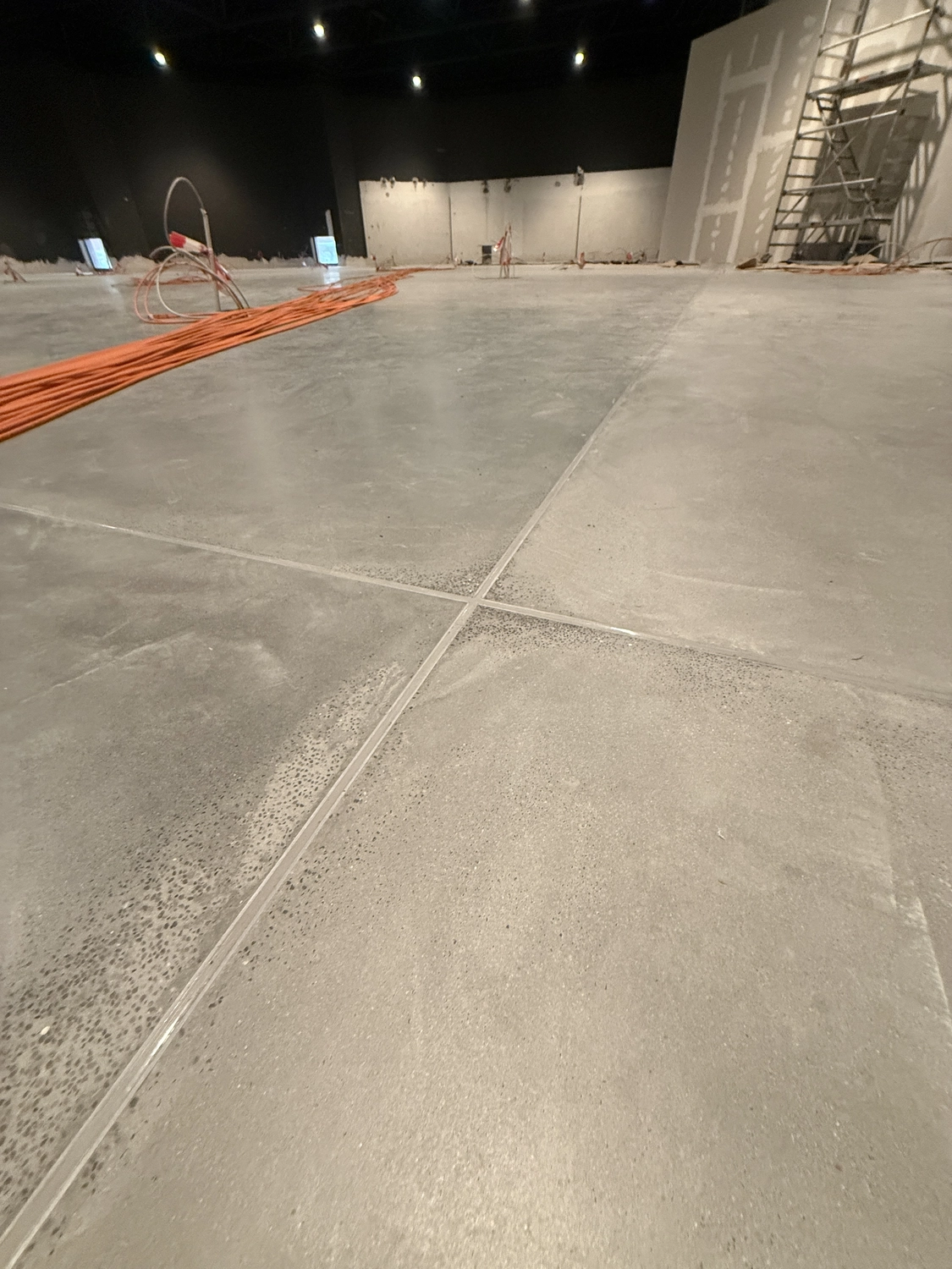 Fugentechnik Buchen - Bau - Baustelleninnenraum mit polierten Betonbodenabschnitten, orangefarbenen Elektrokabeln und Gerüst