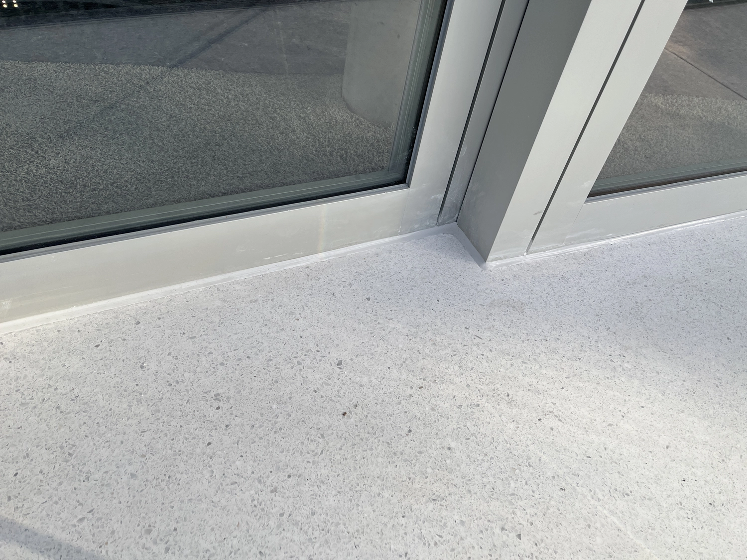 Fugentechnik Buchen - Bau - Nahaufnahme einer Ecke, wo ein grau gesprenkelter Terrazzoboden auf Metallrahmen-Glastüren trifft