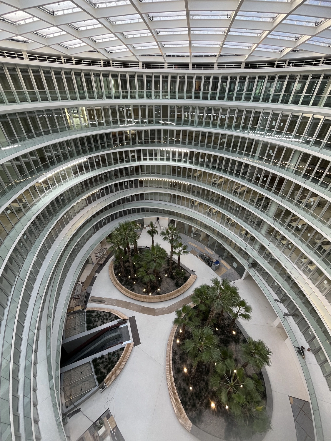 Fugentechnik Buchen - Bau - Innenansicht eines modernen runden Bürogebäudes mit Atrium und mehreren Etagen verglaster Büros, die einen zentralen Garten mit Palmen umgeben