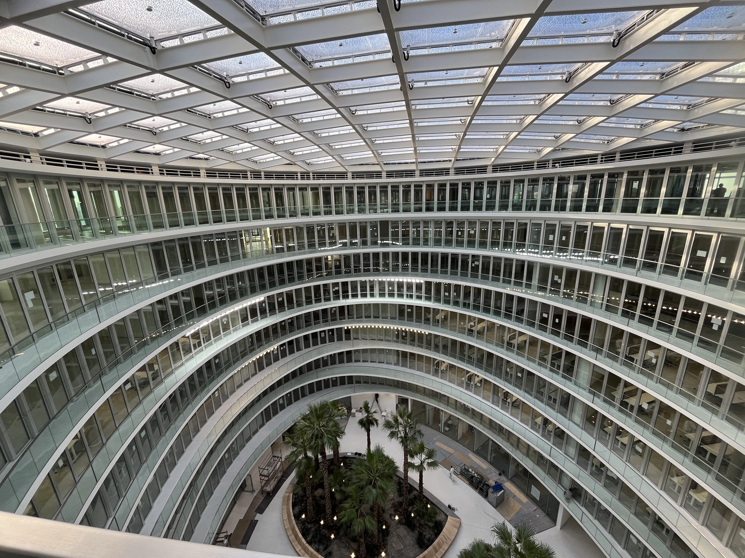 Fugentechnik Buchen - Bau - Innenansicht eines geschwungenen, mehrgeschossigen Bürogebäudes mit verglasten Büros, einem Oberlichtdach und einem Innengarten mit Palmen