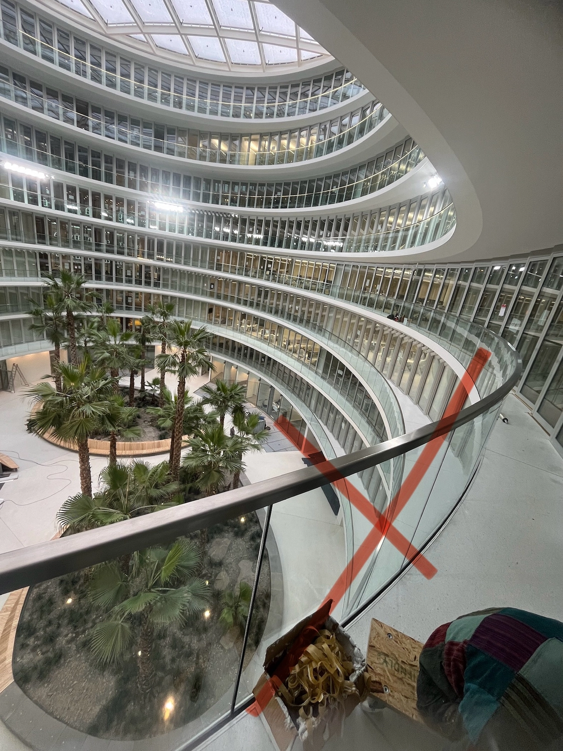 Fugentechnik Buchen – Bau – Innenansicht eines modernen, mehrgeschossigen Bürogebäudes mit zentralem Atrium, das mit Palmen im Innenbereich und geschwungenen Glasbalkonen ausgestattet ist
