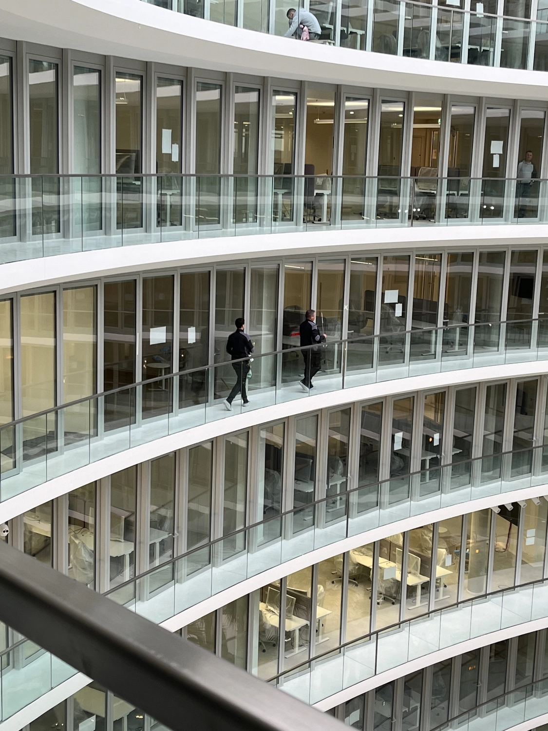 Fugentechnik Buchen - Bau - Innenansicht eines modernen, mehrgeschossigen Bürogebäudes mit gläsernen Gängen und Menschen, die durch die Korridore gehen