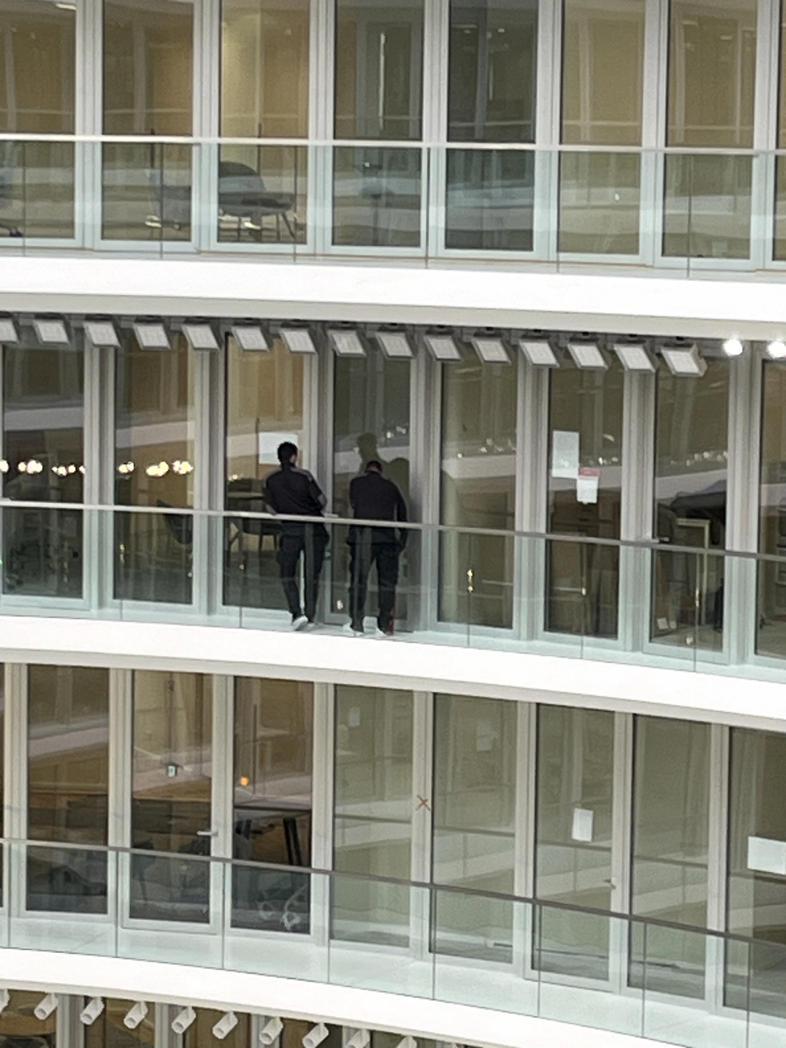 Fugentechnik Buchen - Bau - Zwei Personen stehen und schauen durch Glasfenster auf einem gebogenen Balkon in einem modernen Gebäude