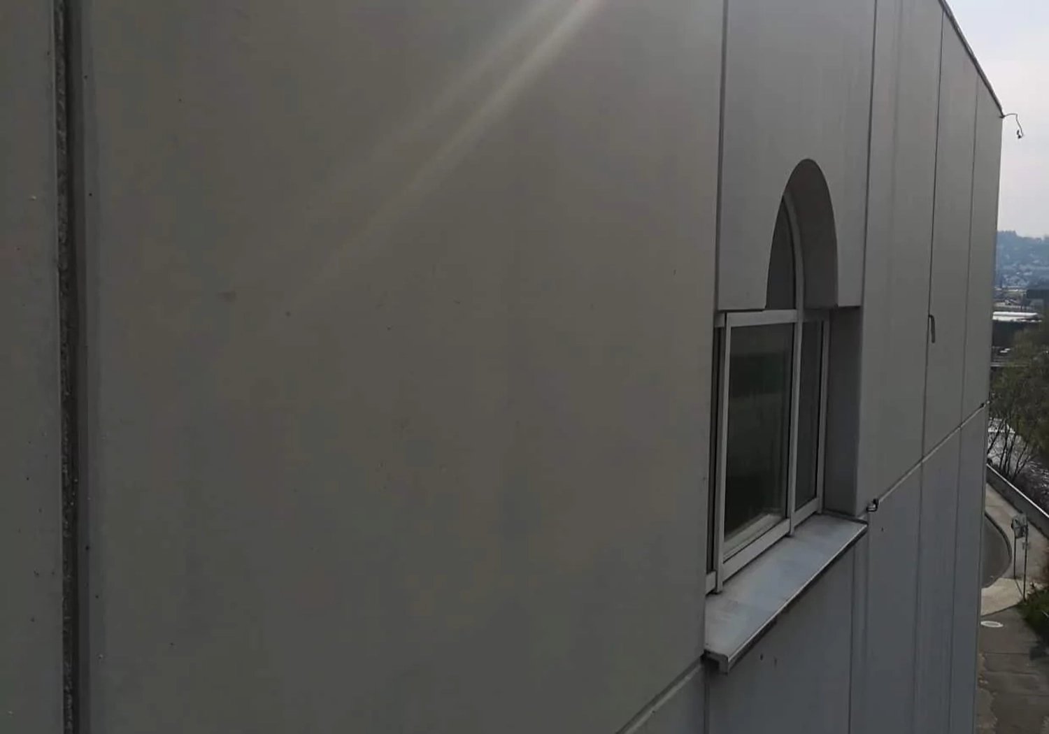 Fugentechnik Buchen - Bau - Außenansicht einer beigefarbenen Gebäudewand mit einem rechteckigen Fenster, das von einem Bogenrahmen bekrönt wird, mit Blick auf eine Straße und die ferne Landschaft