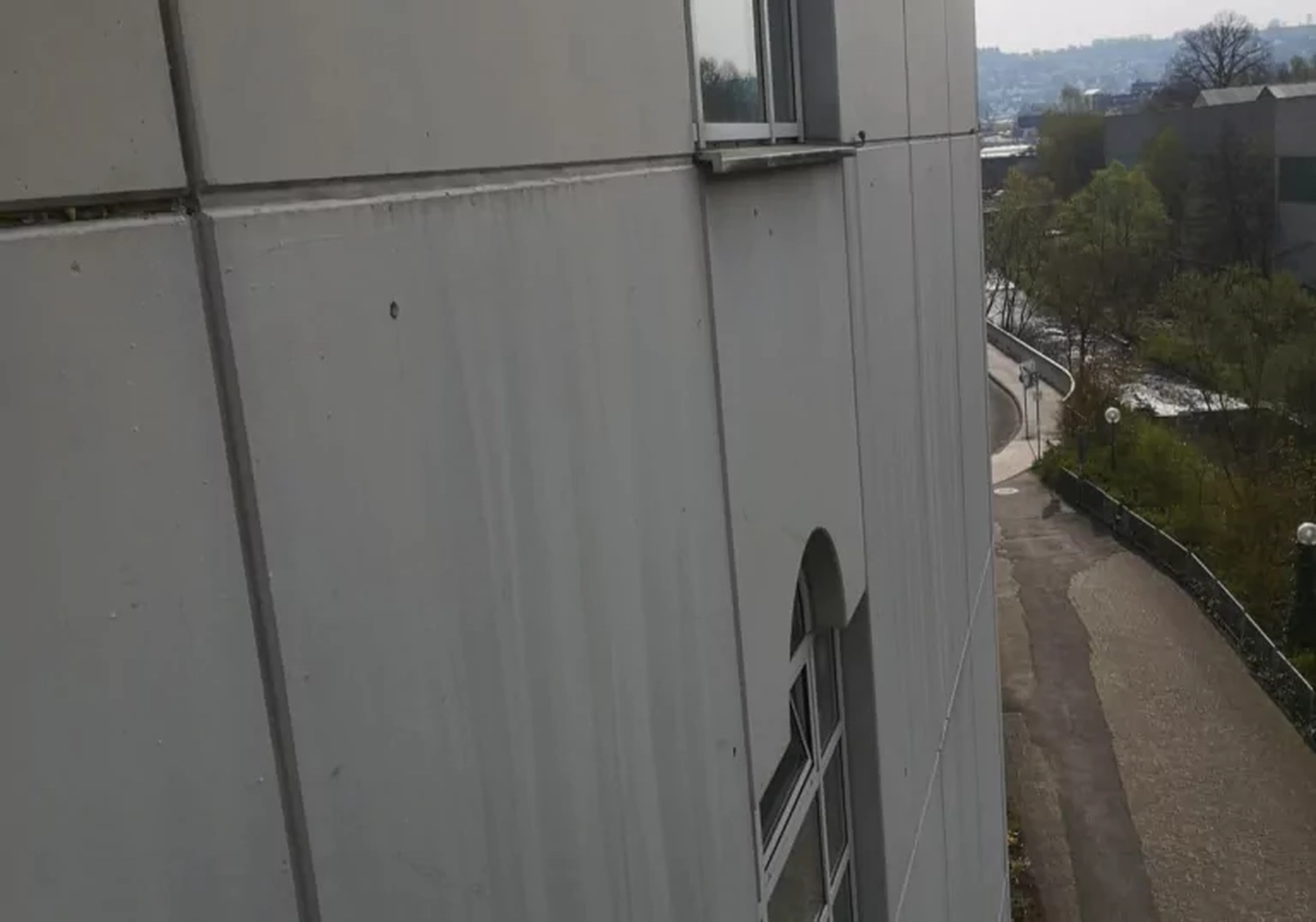 Fugentechnik Buchen - Bau - Blick auf eine graue Betonwand mit Fenstern neben einem geschwungenen Weg und Bäumen