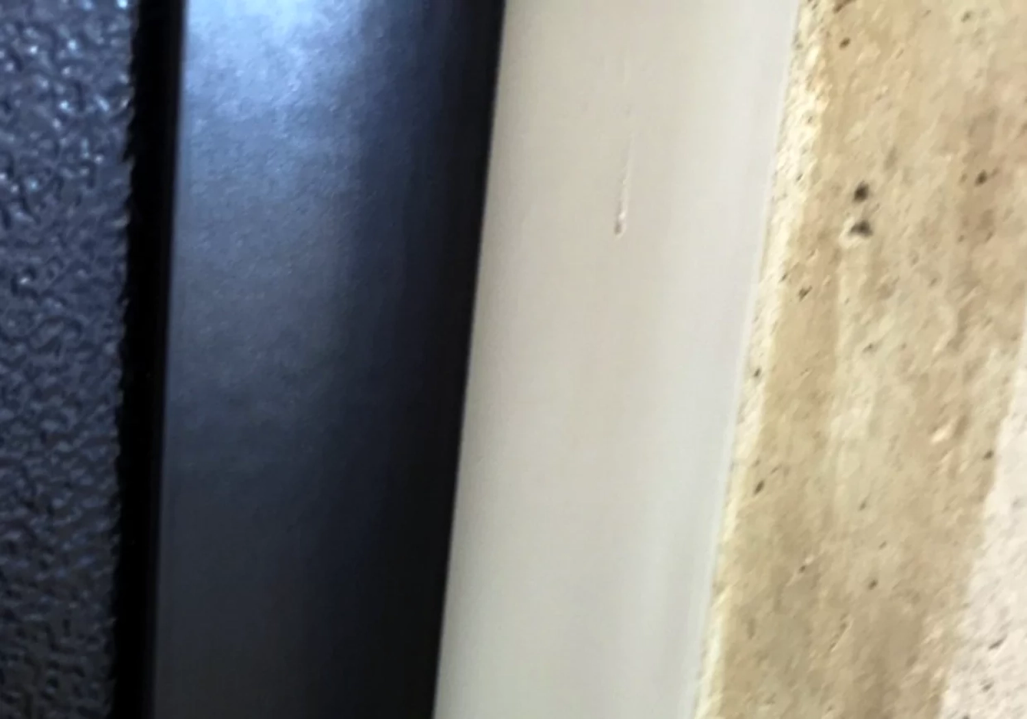 Fugentechnik Buchen - Bau - Nahaufnahme eines schwarzen Türrahmens, einer weißen Wand und einer beigefarbenen, strukturierten Steinoberfläche